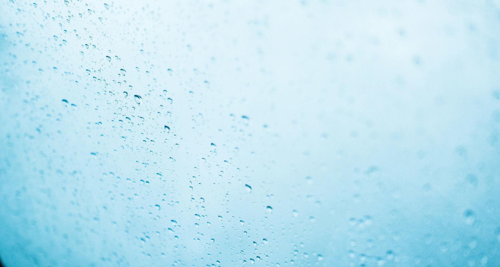 窓ガラスに付着した無数の雨粒と青い空の背景
