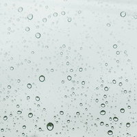 窓ガラスに付いた雨の水滴と雨粒の流れ落ちる様子の写真