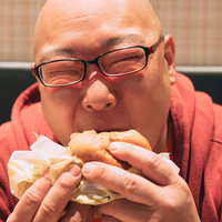 眼鏡をかけた男性がおいしそうにハンバーガーを頬張るの写真