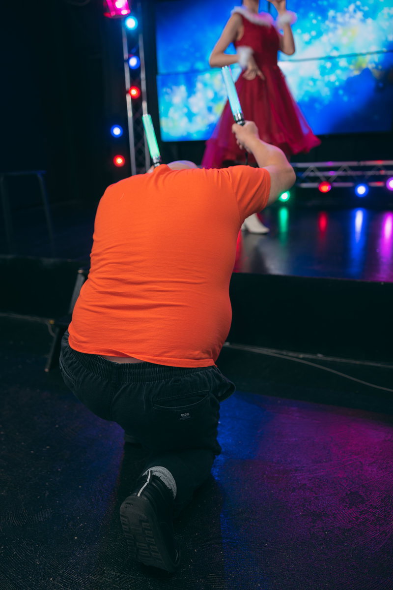 オレンジ色のシャツを着た男性がペンライトを掲げてステージ上のアイドルを応援している［モデル：あまやん モデルリリース］