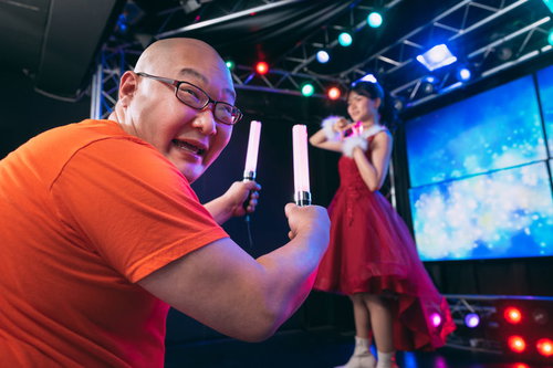 ステージ上のアイドルを熱狂的に応援するペンライトを掲げるファン