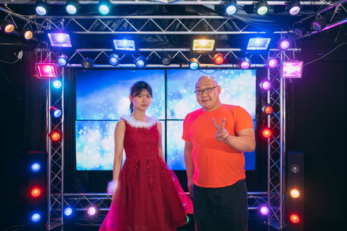 ステージ上のカラフルなライティングでアイドルとツーショットを撮るファン