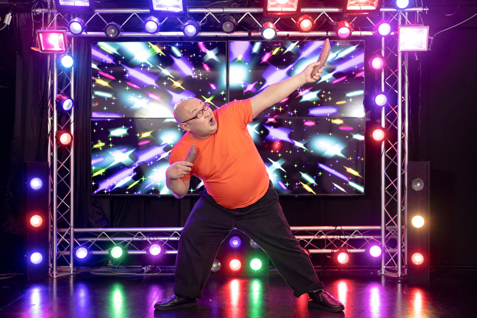 ペンライトが点灯したステージの前で、オレンジシャツの男性がヲタ芸を踊る［モデル：あまやん］
