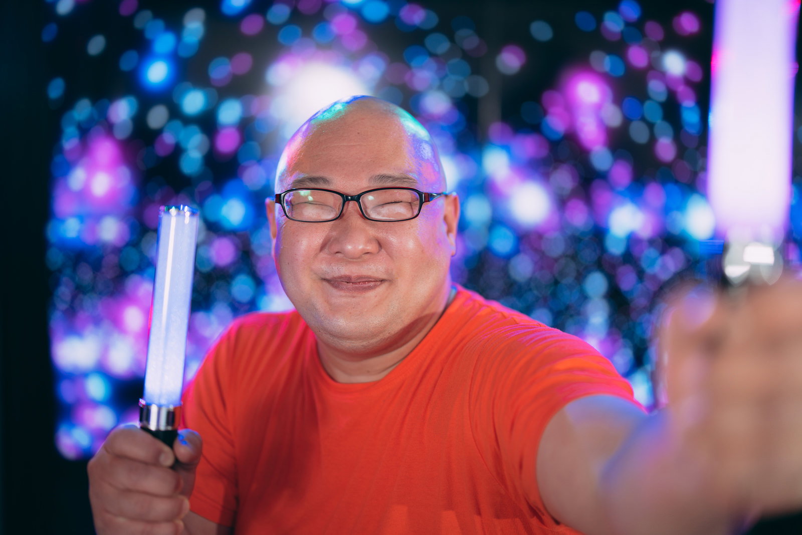 赤いシャツで眼鏡をかけ、ペンライトを握って笑顔の男性［モデル：あまやん］