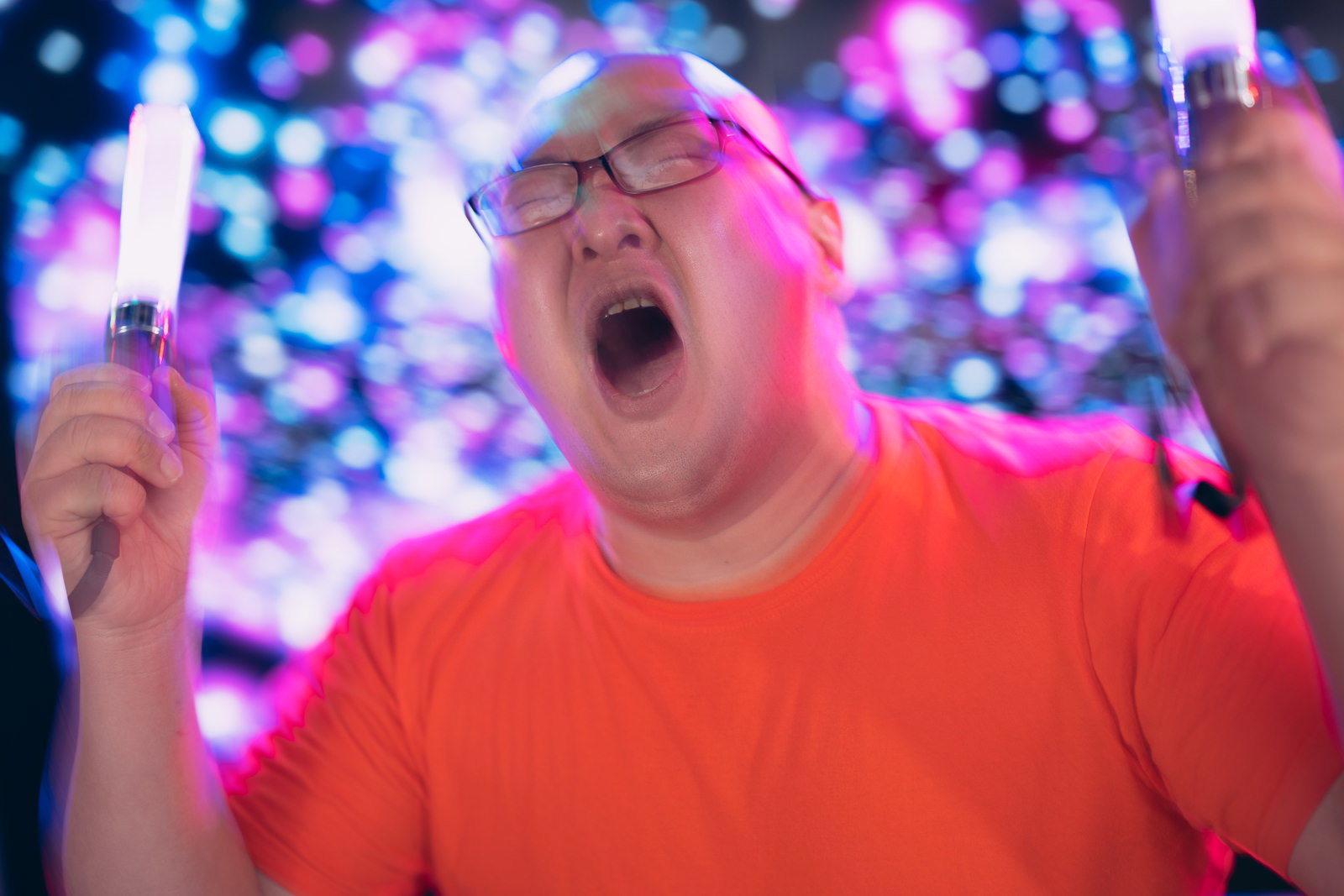 A man in a red shirt shouting while waving a lightstick
