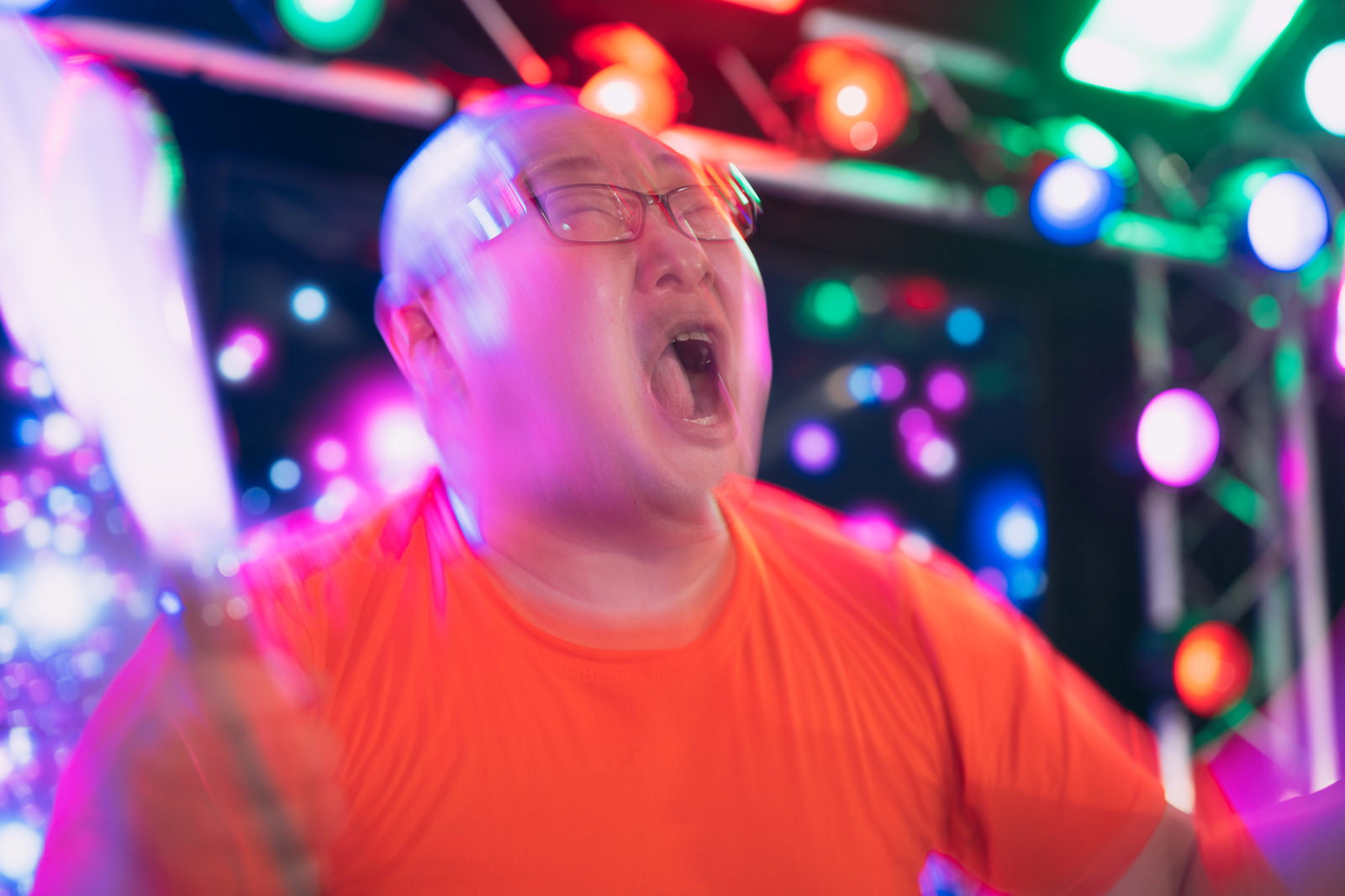 ネオンライトの下でペンライトを持ち、口を開けて声援を送る男性ファン［モデル：あまやん］