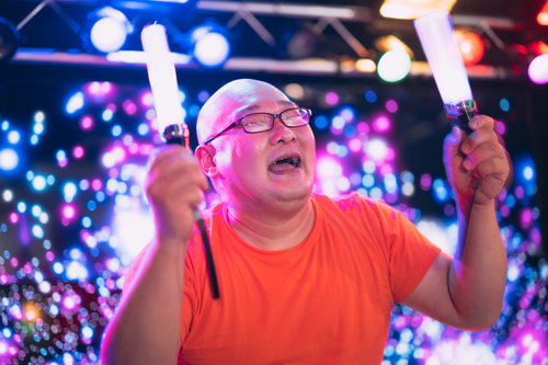 ペンライトを掲げて推し活に熱狂する眼鏡の男性ファン