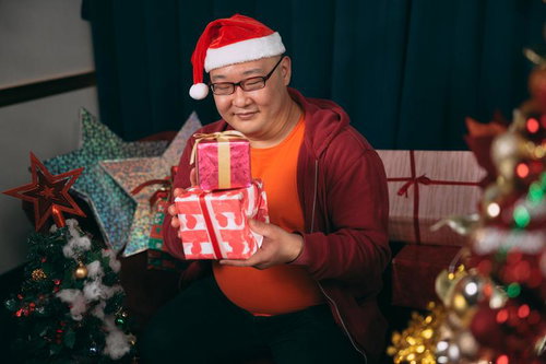 クリスマスプレゼントを手に笑顔の男性、サンタ帽とカジュアルな冬の装い