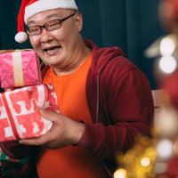 サンタ帽をかぶってクリスマスプレゼントを受け取り喜ぶ男性の写真