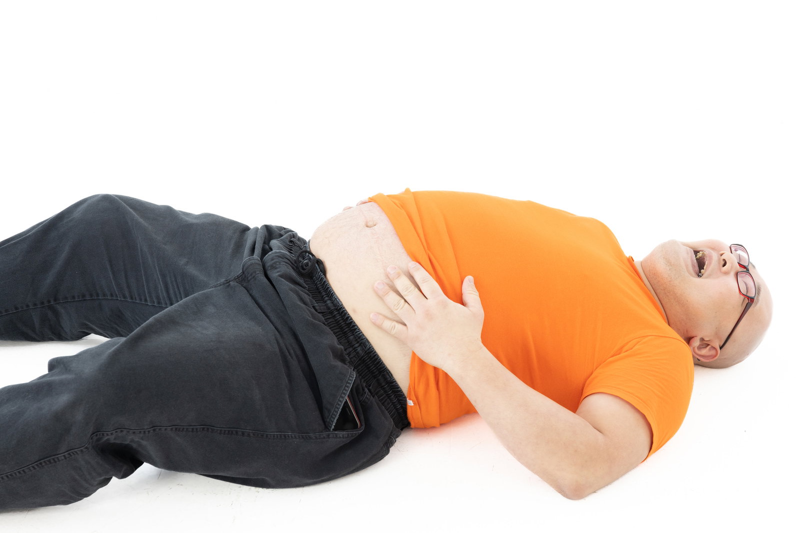 A man in an orange shirt is lying on the floor holding his stomach