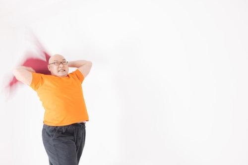 サウナで両腕を振りかぶって熱波を起こすオレンジ色Tシャツの熱波師