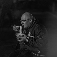寒空の下でカップ麺をすする眼鏡をかけた男性の夜食風景の写真