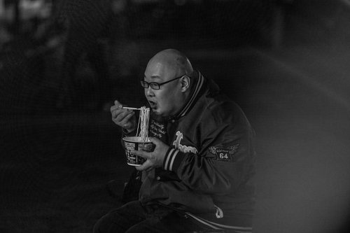 寒空の下でカップ麺をすする眼鏡をかけた男性の夜食風景