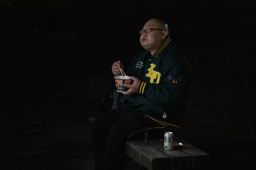 カップ麺を食べて眼鏡が曇る男性の夜間の情景
