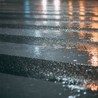 雨に濡れた横断歩道に映る街灯の光と水たまりの反射の写真