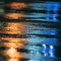 雨で濡れたアスファルトに映り込むネオンの光と反射の写真