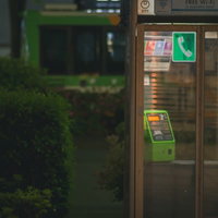 雨粒に濡れる緑色の電話ボックスの写真