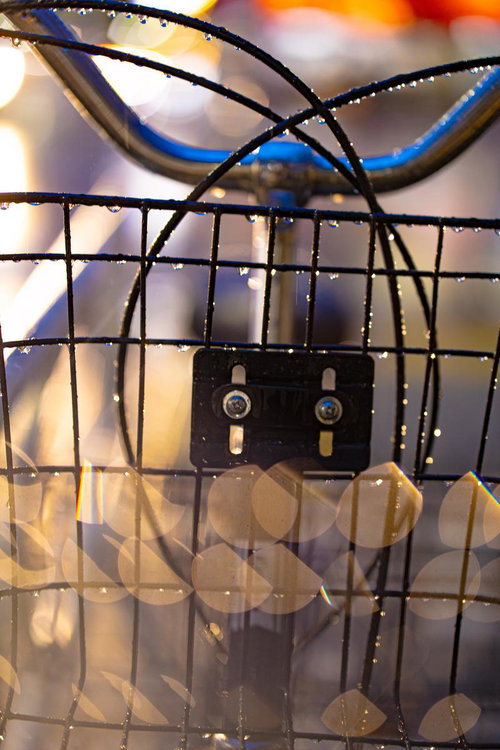 夜の雨に濡れた自転車の前バスケットと街灯の光が映る水滴