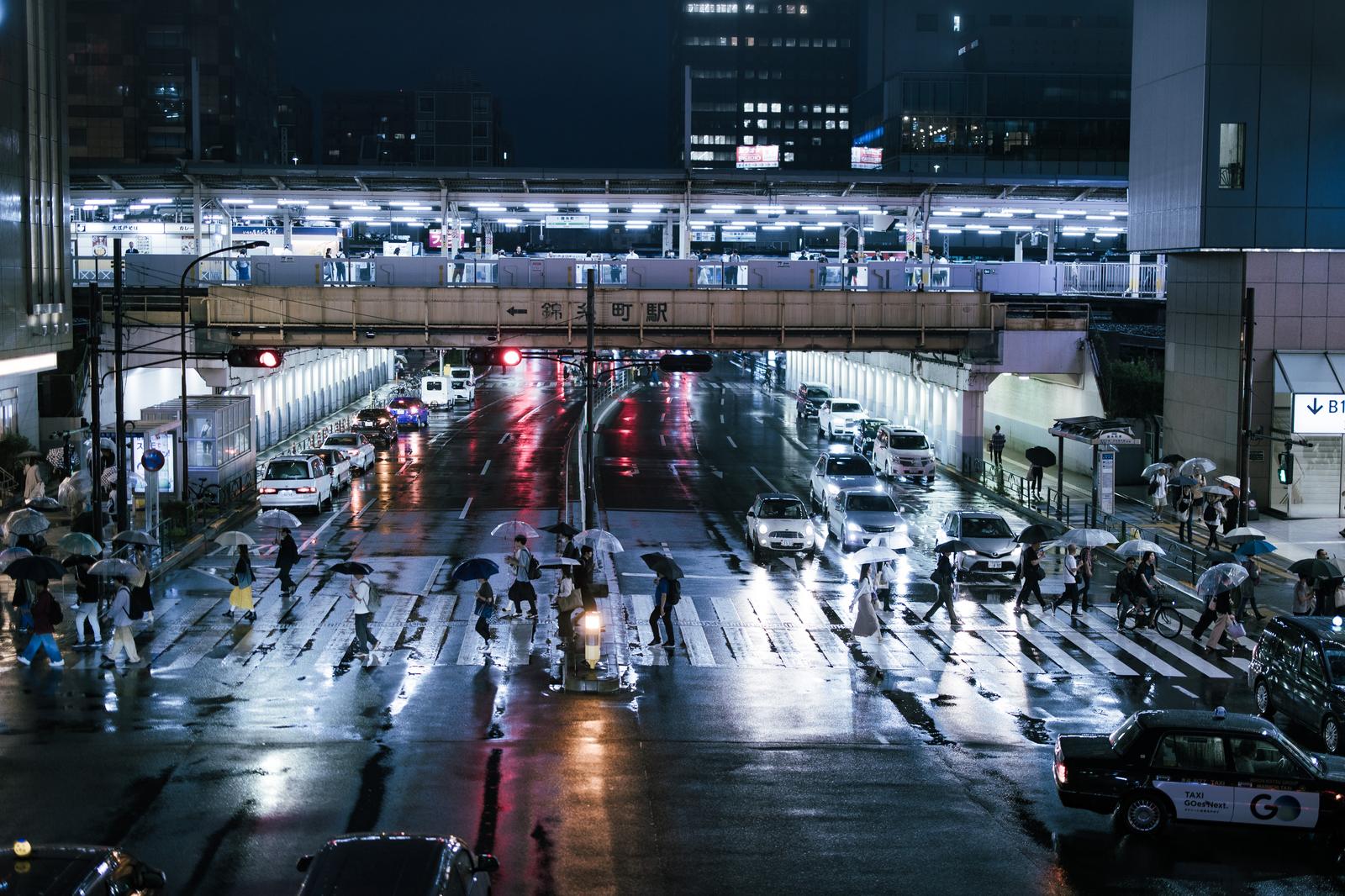 夜間の雨上がり、錦糸町駅前の横断歩道を渡る人々と濡れた路面