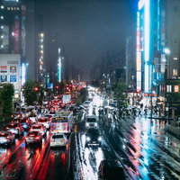 雨で濡れた夜の都市交差点、ネオン看板とテールランプが彩る梅雨の車道の写真
