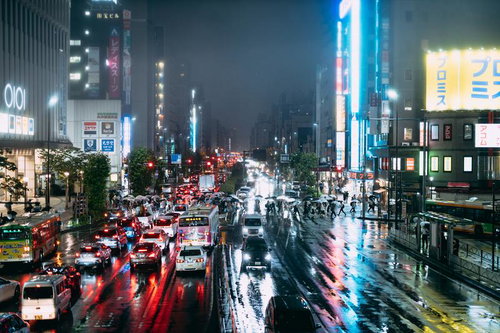雨で濡れた夜の都市交差点、ネオン看板とテールランプが彩る梅雨の車道