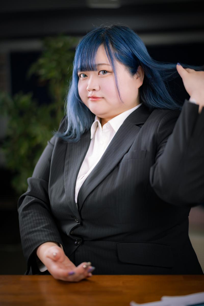黒いビジネススーツを着た青髪の女性が髪をかき上げている［モデル：あねちゃん］