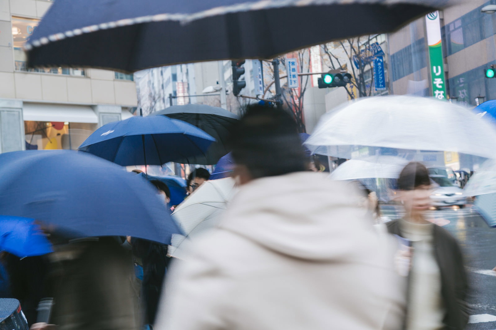 雨の日に青や黒の傘をさして歩く複数の歩行者