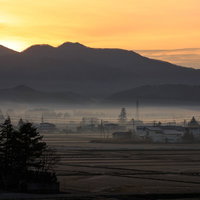 霧がかかる田舎の夜明け、山並みと民家のシルエットの写真