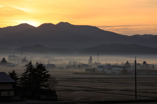 霧がかかる田舎の夜明け、山並みと民家のシルエット