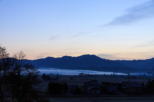 霧の中の朝焼けに包まれた田舎の風景、山々と民家