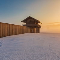 朝霧に包まれた雪原の払田柵跡の復元建物と朝焼けの空の写真