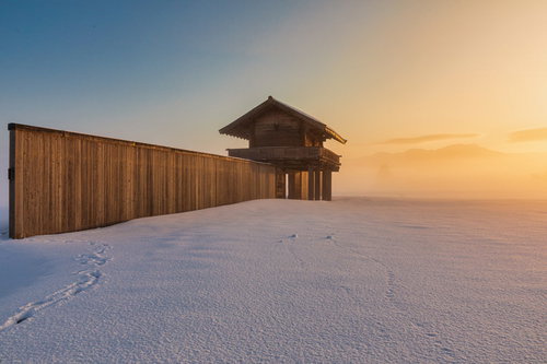 朝霧に包まれた雪原の払田柵跡の復元建物と朝焼けの空