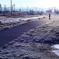 冬の朝、工業地帯の河川沿いを歩く人物の写真