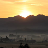 霧に包まれる田舎町の夜明け - 山並みと田んぼの写真