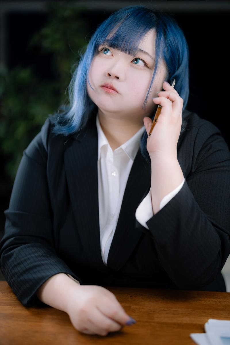 スーツを着た青髪の女性がスマートフォンで通話している