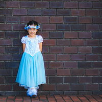白い花飾りをつけた青いドレスの女の子がレンガ壁の前で笑顔の写真