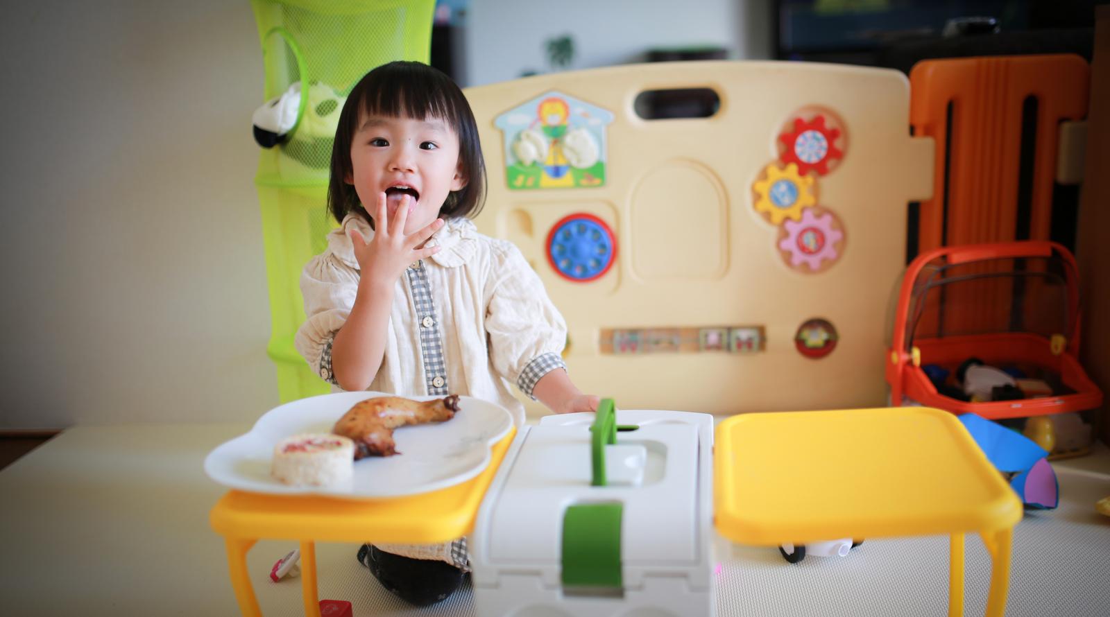 Young girl smiling and sticking out her tongue while eating a snack at a beige table