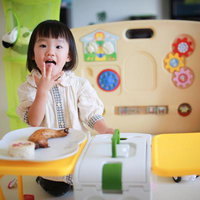 保育園の室内で知育玩具に囲まれておやつを食べる幼い女の子の写真