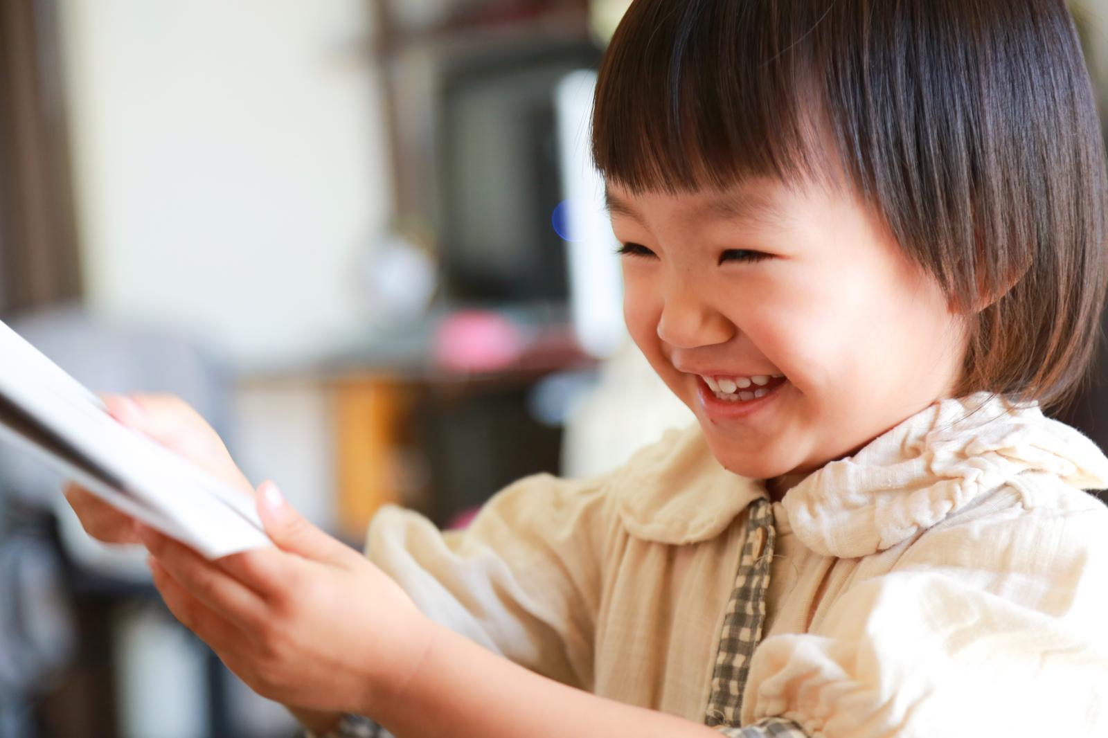 Girl smiling while looking at a tablet. She is wearing a beige-colored outfit.