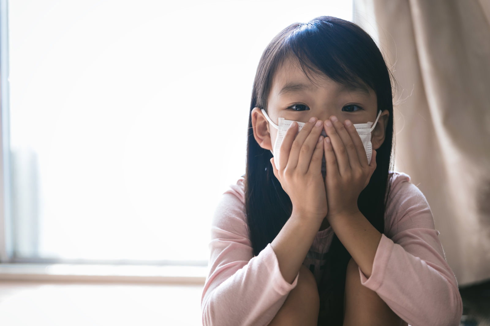 両手でマスクを押さえるピンクの服を着た女の子［モデル：あんじゅ］