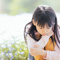 お花畑でうつむく女の子の不安そうな表情と心理状態の写真