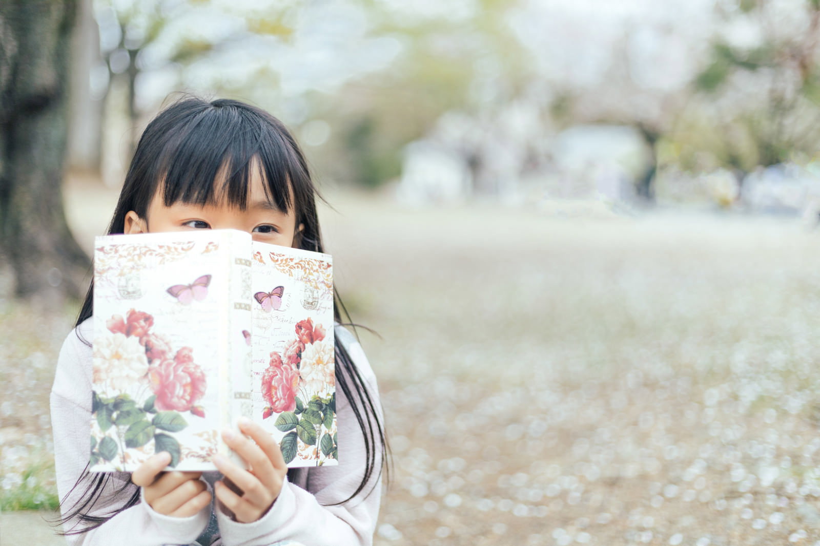 桜咲く公園で花柄の聖書を読む黒髪の女の子［モデル：あんじゅ］
