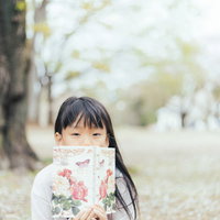 公園のベンチで洋書を広げて読書する女の子の写真