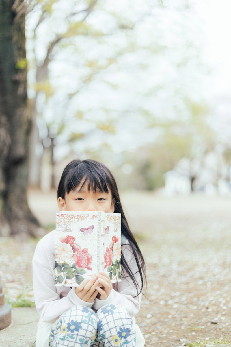 公園のベンチで洋書を読む女の子［モデル：あんじゅ］