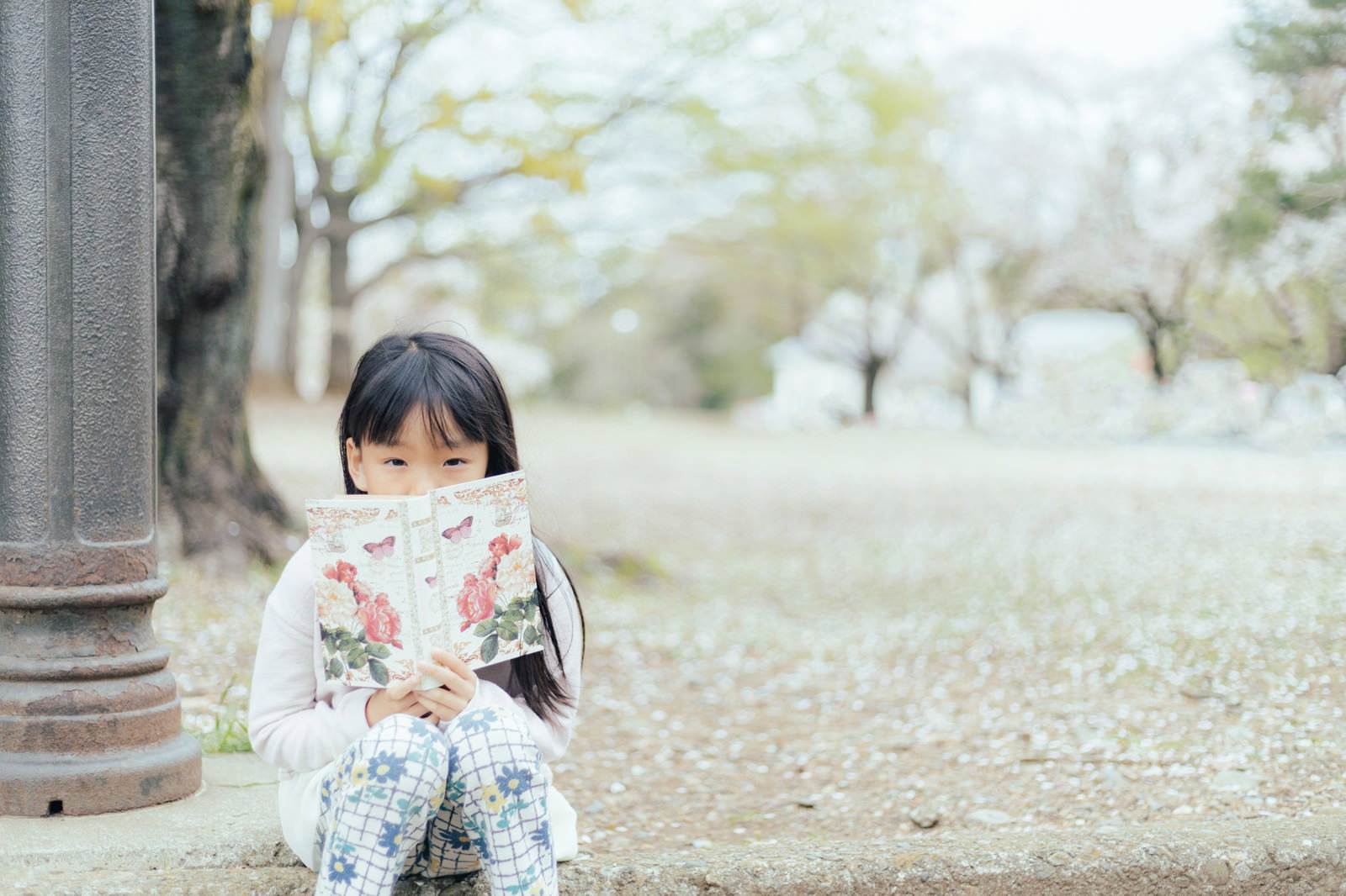 公園の木の根元に座って洋書を読んでいる女の子［モデル：あんじゅ］