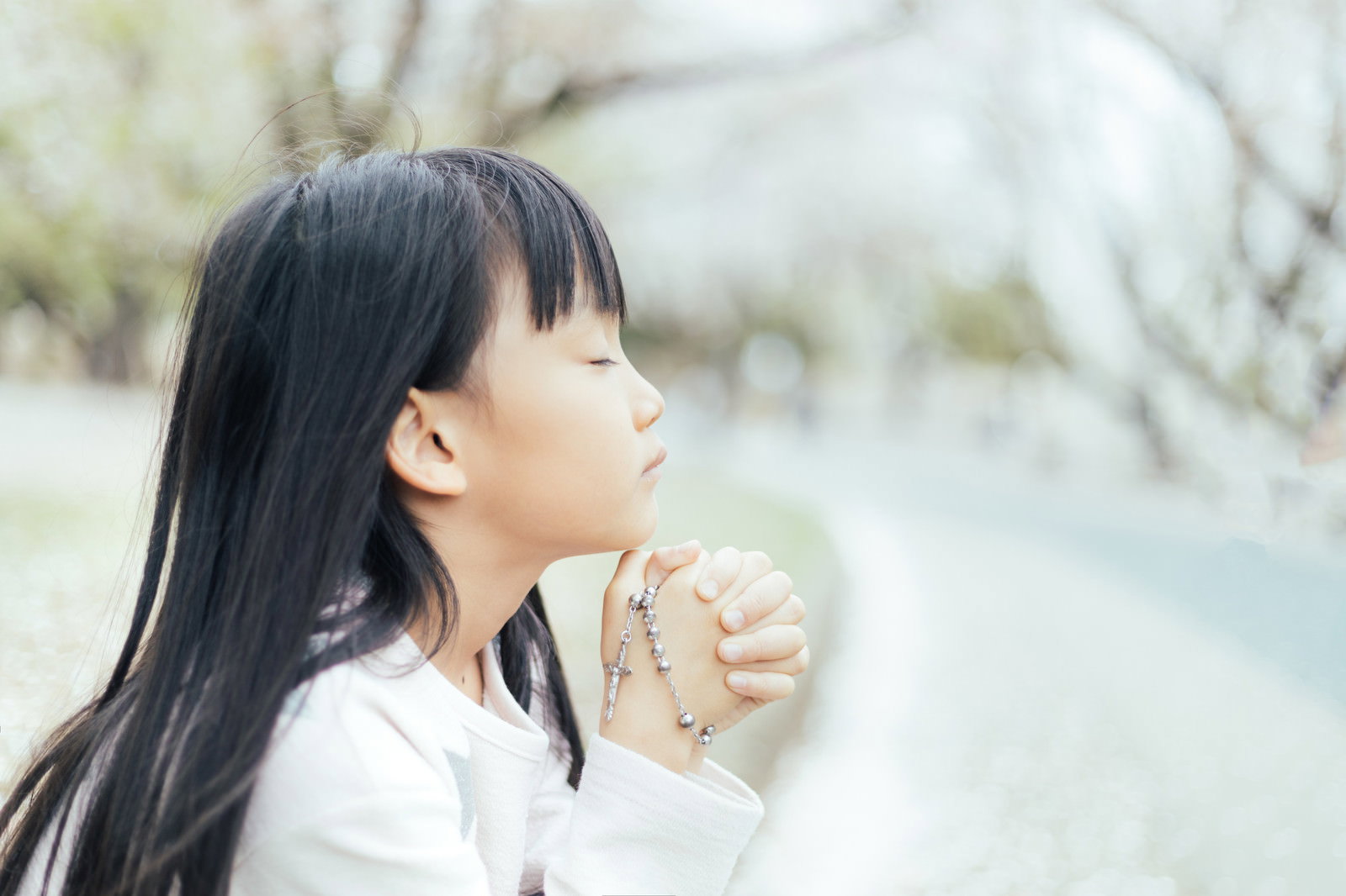 ロザリオを両手で握りしめて祈りを捧げる白い服を着た女の子［モデル：あんじゅ］