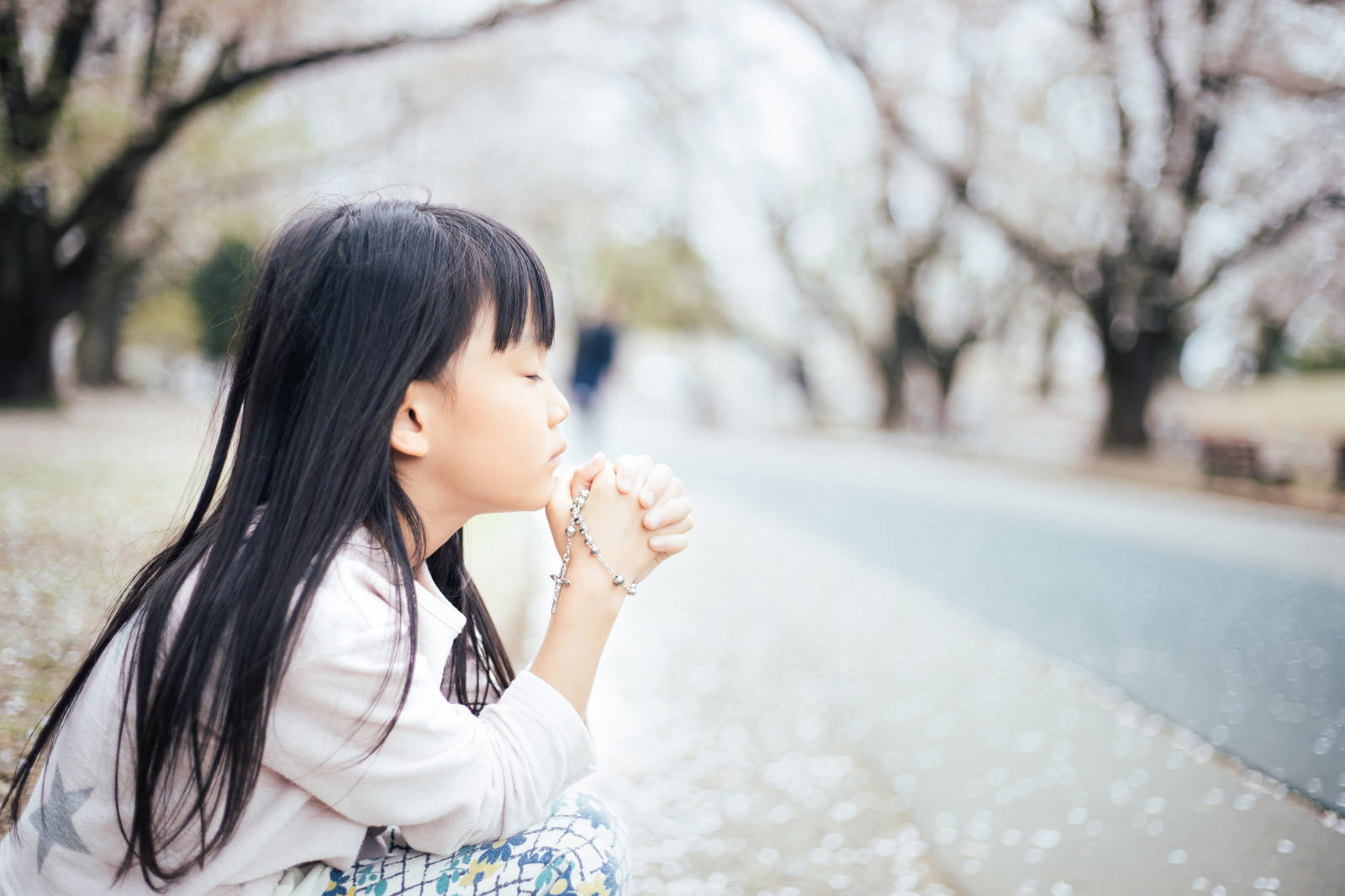 桜並木の道でロザリオを握り締めて祈る黒髪の女の子［モデル：あんじゅ］