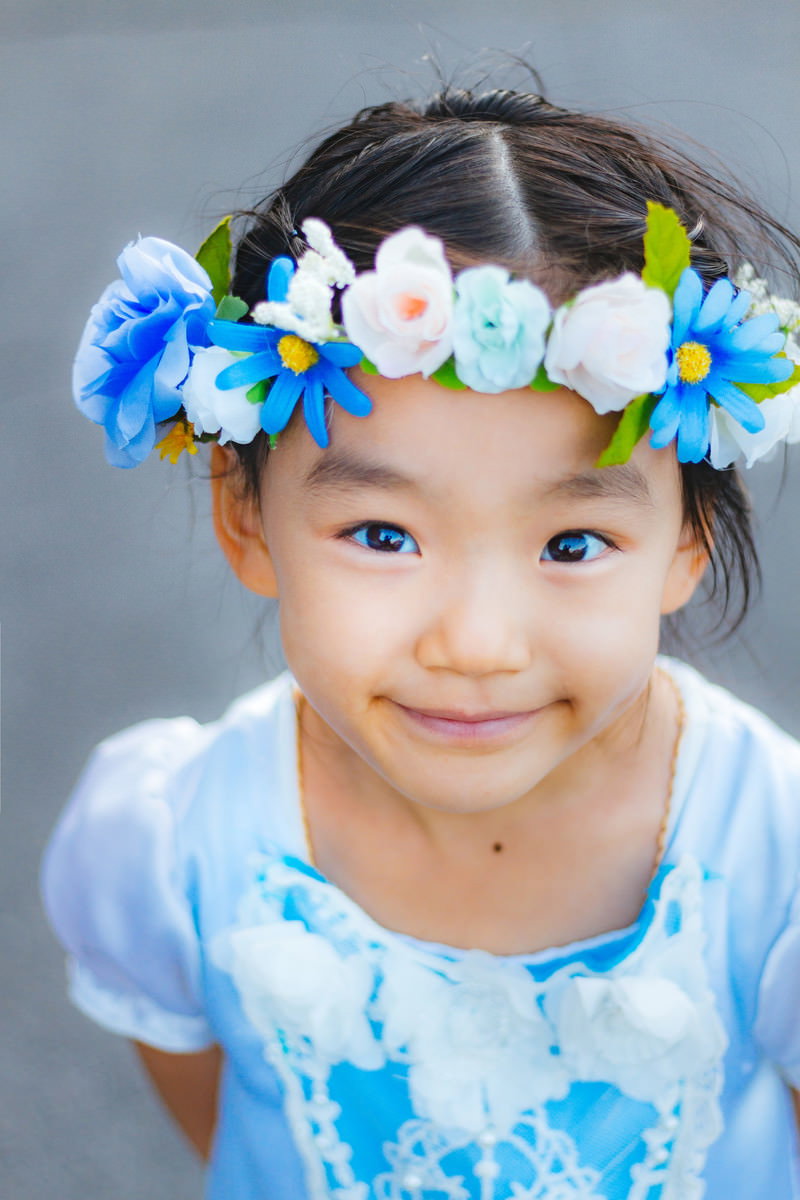 青と白の花飾りを頭に着けて笑顔を見せる青い服の女の子［モデル：あんじゅ］