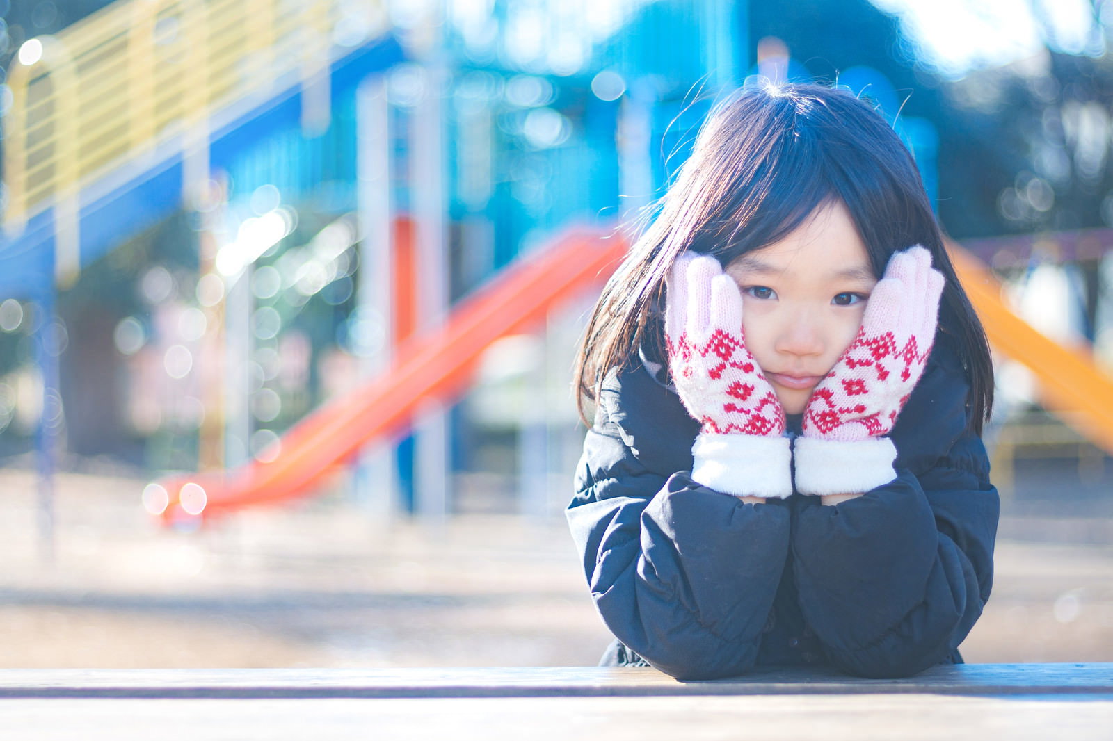 公園のすべり台の前で寒そうにほっぺたをおさえる女の子［モデル：あんじゅ］