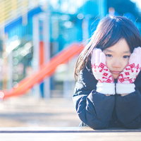 公園のすべり台の前で寒くてほっぺをおさえる女の子の写真